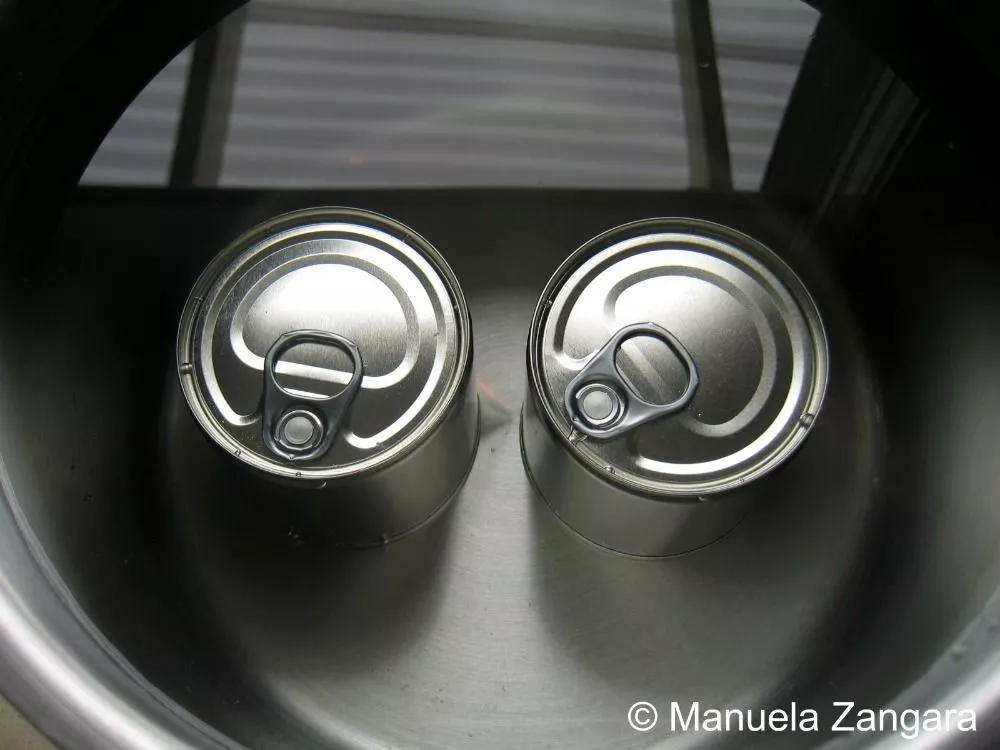 Two tins of condensed milk submerged in a pot of water.