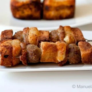Fried Sicilian meatball spiedini skewers arranged on a white plate with golden bread and salami layers.