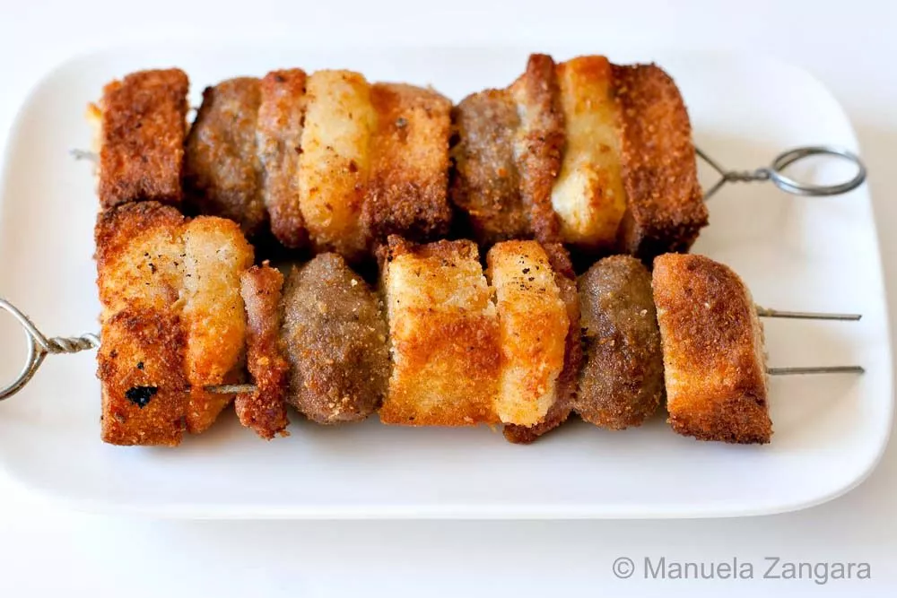 Crispy Sicilian meatball spiedini skewers with golden bread and cheese layers served on a white plate.