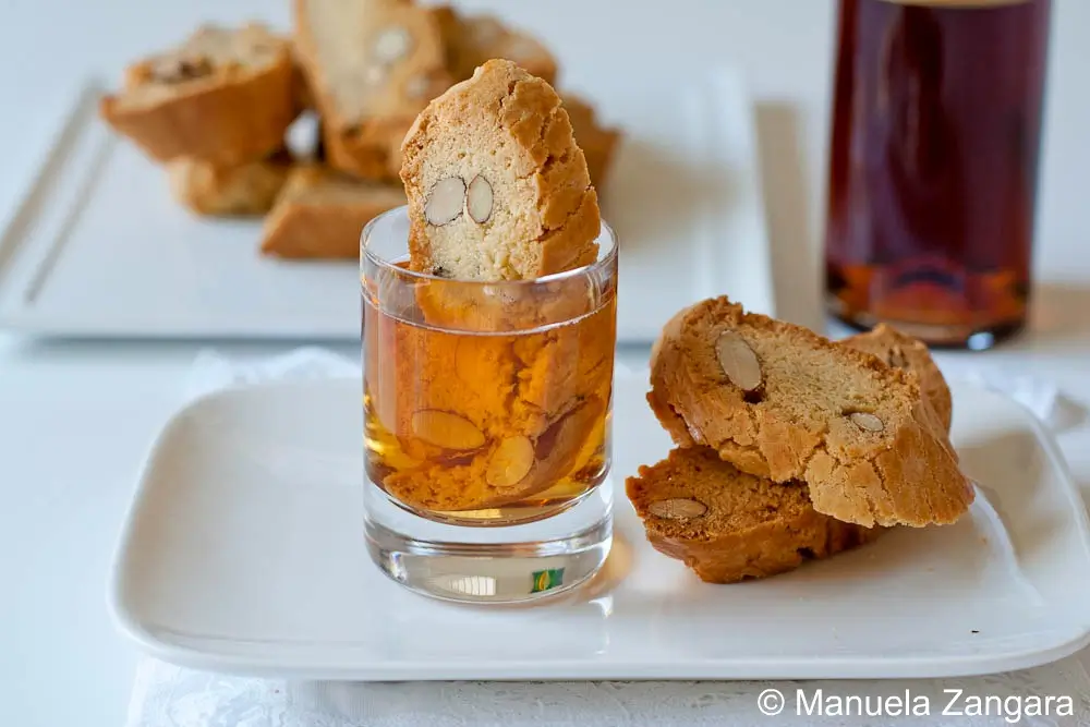 Almond cantucci dipped into a small glass of sweet wine on a white plate.
