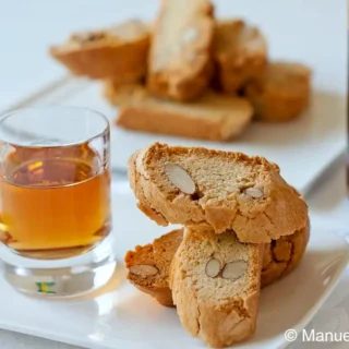 Cantucci slices on a plate beside a glass of sweet wine and a bottle in the background.
