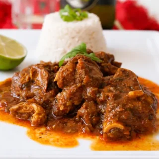Chivo Guisado served with white rice and lime on a plate.