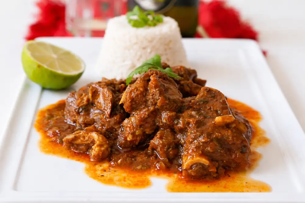 Chivo Guisado served with white rice and lime on a plate.