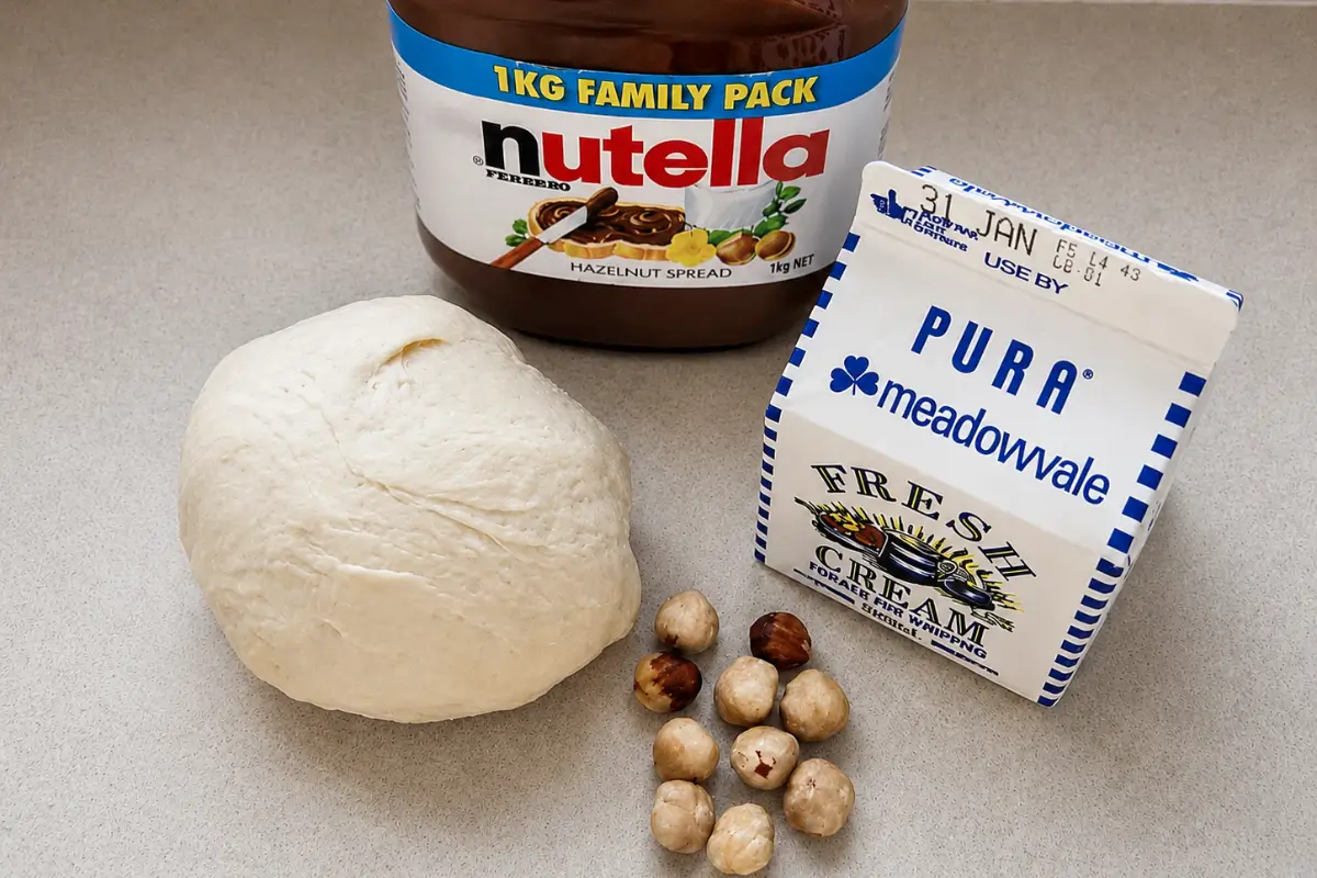 Pizza dough, Nutella, whipped cream, and toasted hazelnuts arranged on a kitchen counter.