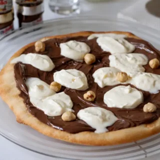 Slice of Nutella Pizza topped with whipped cream and toasted hazelnuts on a white plate.