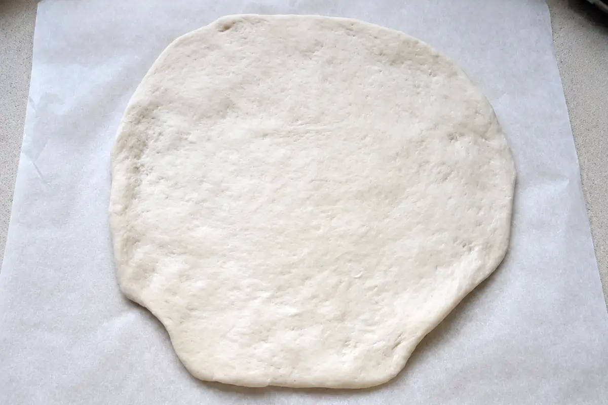 Rolled pizza dough on parchment paper before baking.