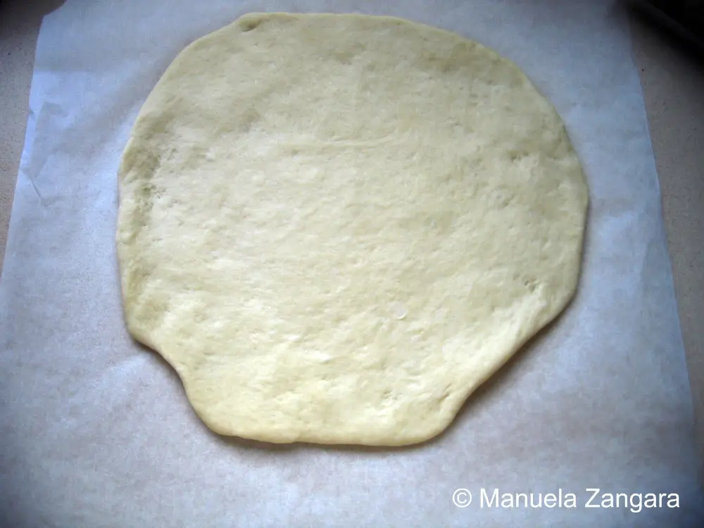 Rolled pizza dough shaped into a round on parchment paper before baking.