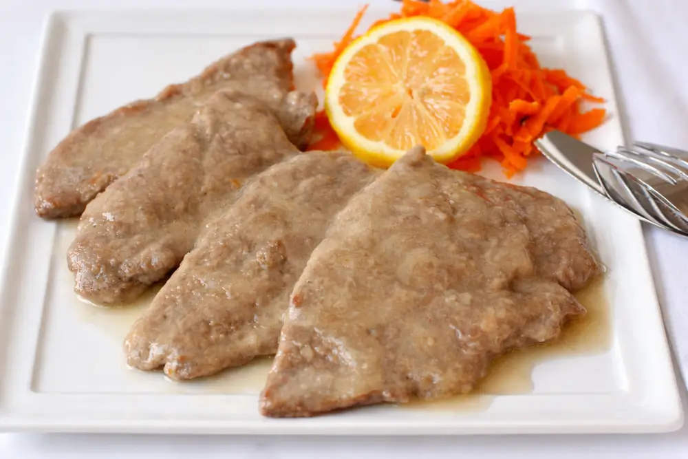 Scaloppine al Limone served with a light lemon sauce and sliced lemon on a white plate.