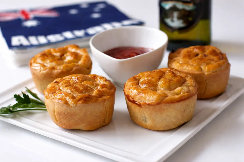 Freshly baked mini beef pies served on a plate with ketchup on the side.