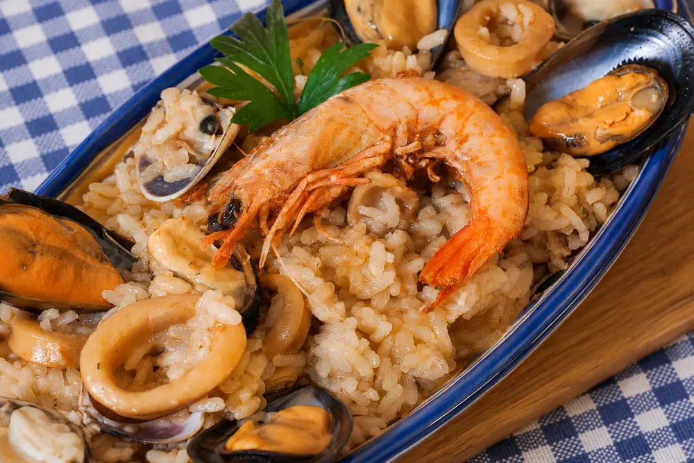 Seafood risotto served on an oval plate with mussels, clams, calamari, and whole prawns.