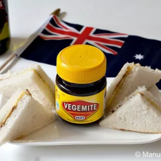 Vegemite and cheese sandwiches served with an Australian flag and a bottle of beer in the background.