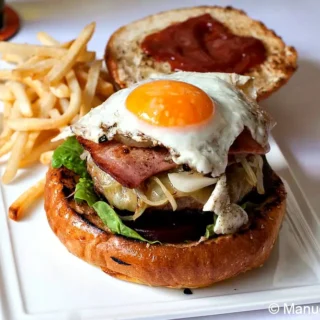 Fully assembled Aussie Burger with the Lot on a plate with fries and ketchup spread on the top bun.