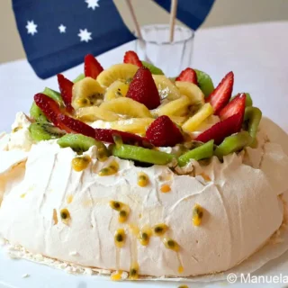Pavlova decorated with whipped cream and fresh fruit.