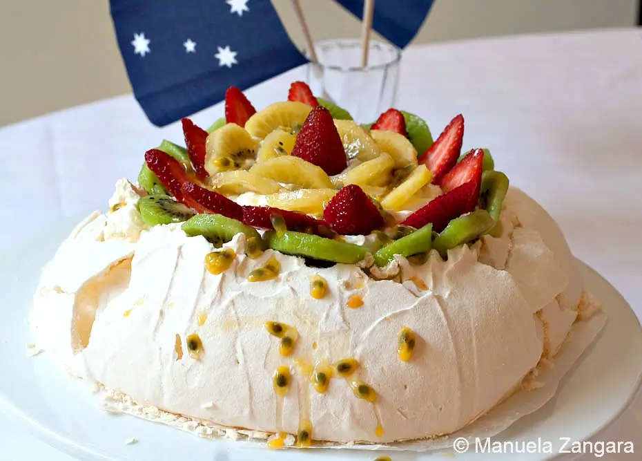 Pavlova decorated with whipped cream and fresh fruit.