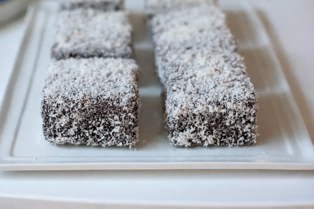 Classic coconut lamingtons arranged in rows on a white serving plate.