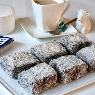 Classic lamingtons coated in chocolate icing and rolled in desiccated coconut on a serving plate.