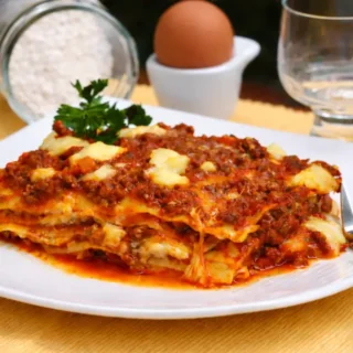 Lasagna portion served on a plate with sauce and melted cheese.
