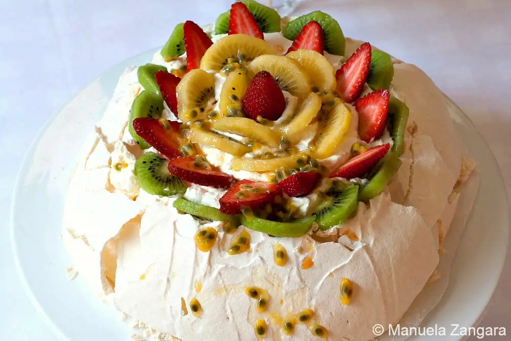 Pavlova served on a cake stand with fresh fruit topping.