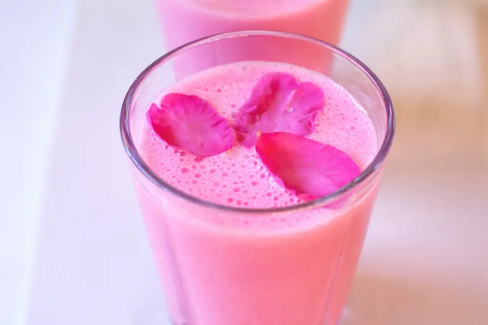 Close-up of a glass of pink lassi with rose petals floating on top.
