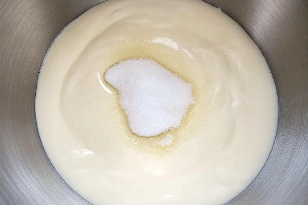 Caster sugar added to beaten egg whites in a mixing bowl.