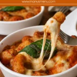 Baked gnocchi with golden mozzarella, tomato sauce, and basil in a white dish.