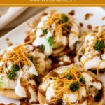 Papri Chaat topped with yoghurt, chutneys, potatoes, chickpeas, and sev on a serving plate.