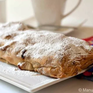 Baked Apple Strudel covered with powdered sugar on a white serving plate.