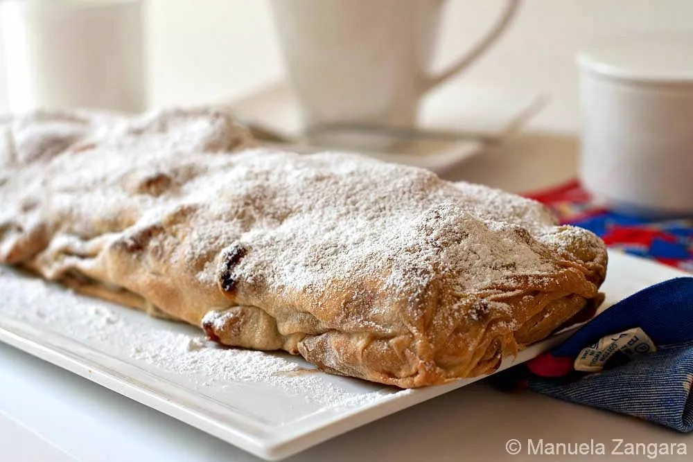 Baked Apple Strudel covered with powdered sugar on a white serving plate.