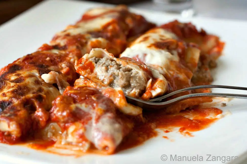 Baked Cannelloni di Carne topped with tomato sauce and melted cheese, with a fork cutting into the meat filling.