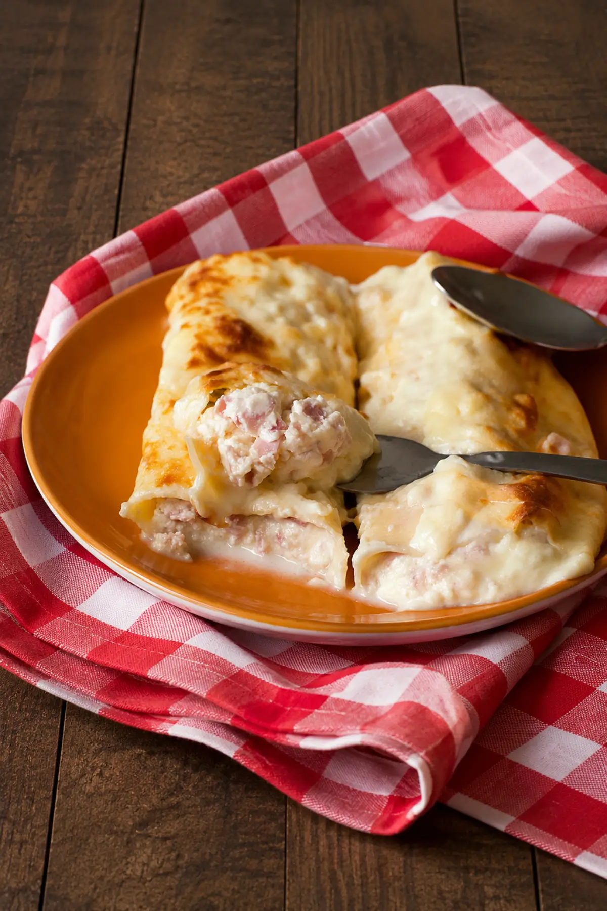 Cannelloni filled with ricotta, ham, and Fontina cheese served on a plate with creamy béchamel sauce.