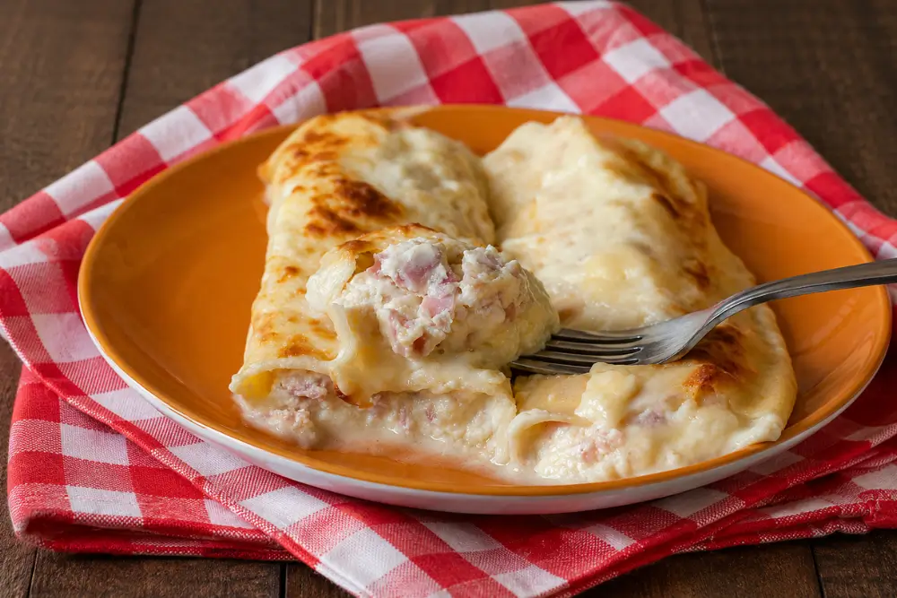 Fork holding a bite of cannelloni with a creamy ricotta, ham, and Fontina filling.