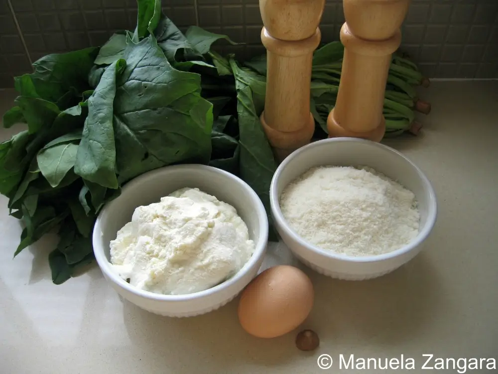Fresh spinach, ricotta, Parmigiano Reggiano, egg, and nutmeg on a countertop.