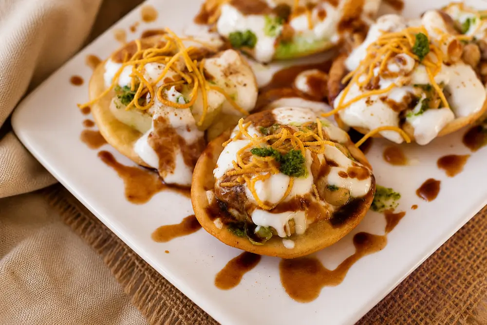 Close-up of papri chaat topped with yoghurt, tamarind chutney, hari chutney, potatoes, chickpeas, and sev.