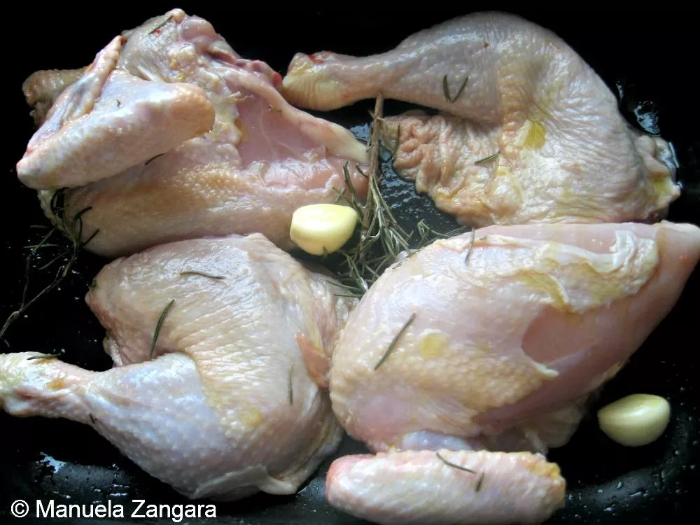 Raw chicken pieces tossed with olive oil, rosemary, and garlic in a baking dish.