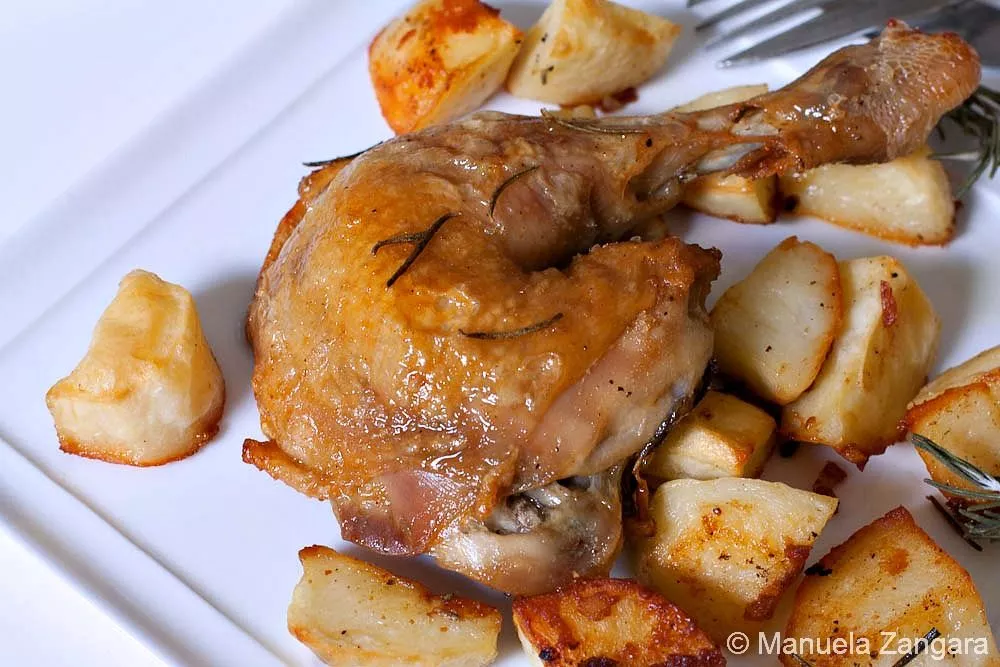 Close-up of roasted chicken leg with crisp potatoes and rosemary on a white plate.