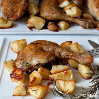 Roasted chicken leg served with golden potatoes on a white plate with rosemary garnish.