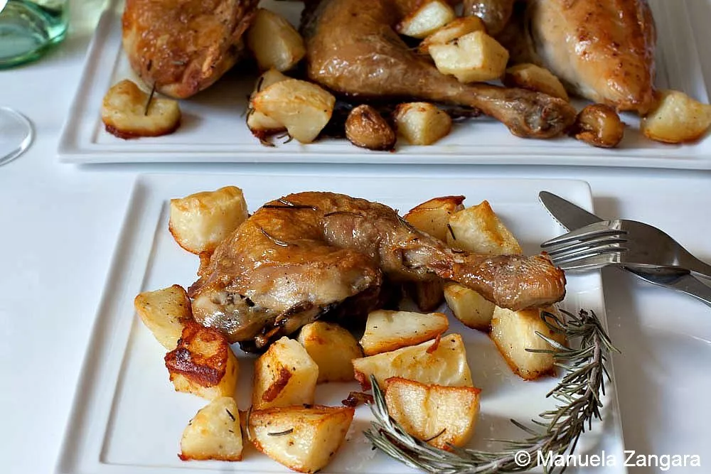 Roasted chicken leg served with golden potatoes on a white plate with rosemary garnish.