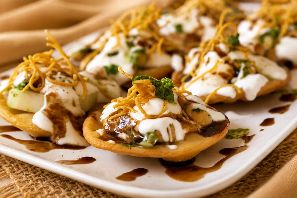 Homemade papri topped with yoghurt, chickpeas, potatoes, chutneys on a plate.