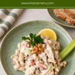 Creamy chicken salad with celery and walnuts on a sage-green plate, served with lemon, celery and sliced bread.