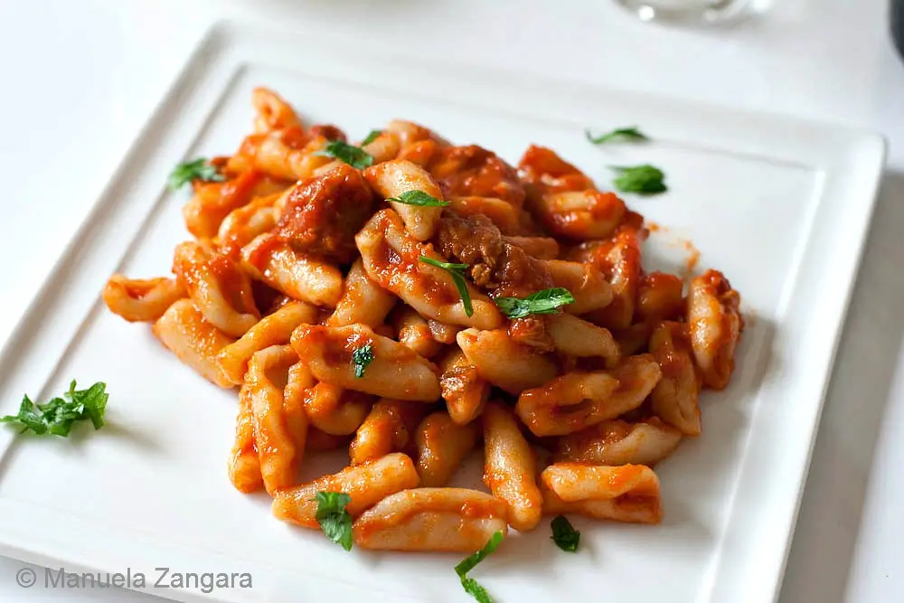 A plate of cavatelli coated in pork ragù and topped with small pieces of parsley.