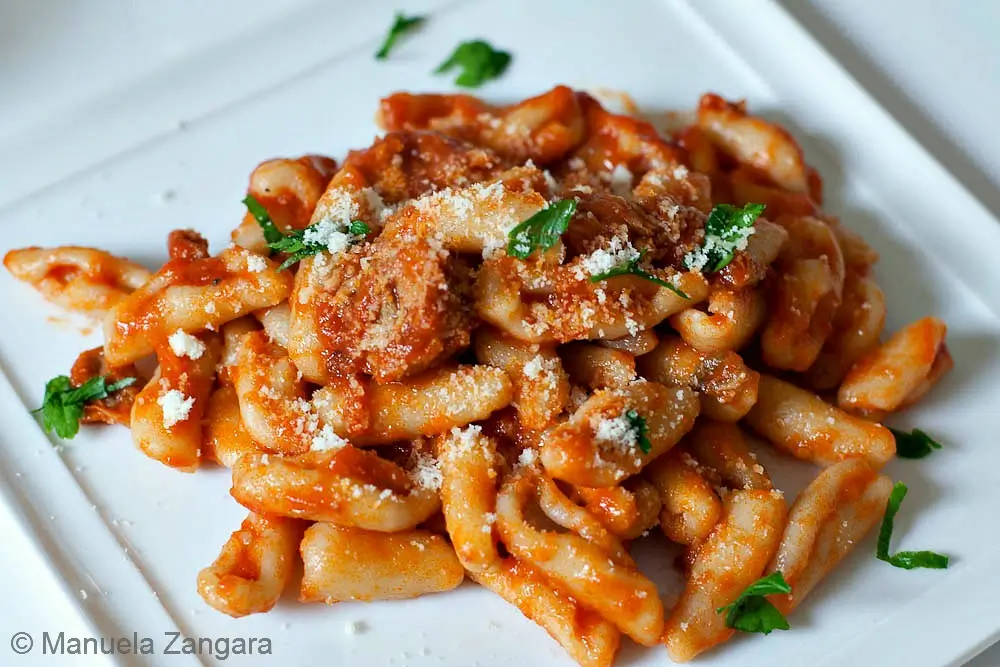 Cavatelli con ragu' di maiale A plate of cavatelli coated in pork ragù and topped with grated cheese and parsley.