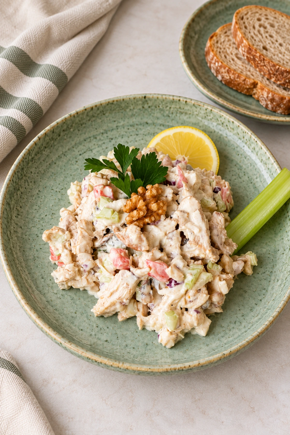 Creamy shredded chicken with celery and red onion on a sage-green plate, garnished with walnuts and parsley.