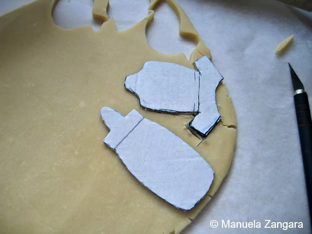 Cutting cookie dough into baby bottle and onesie shapes for Baby Shower Shortbread Cookies using paper templates.