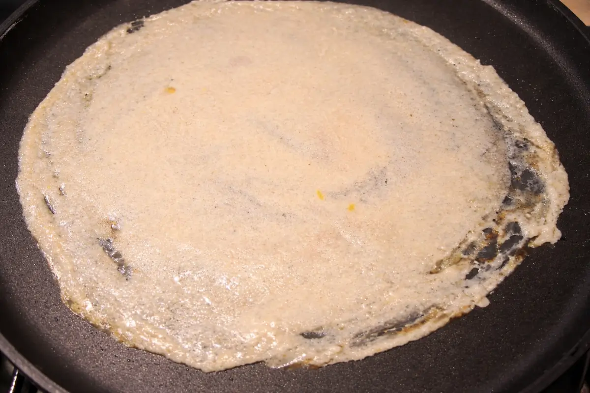 Dosa batter spread thinly across a hot pan forming an even layer.
