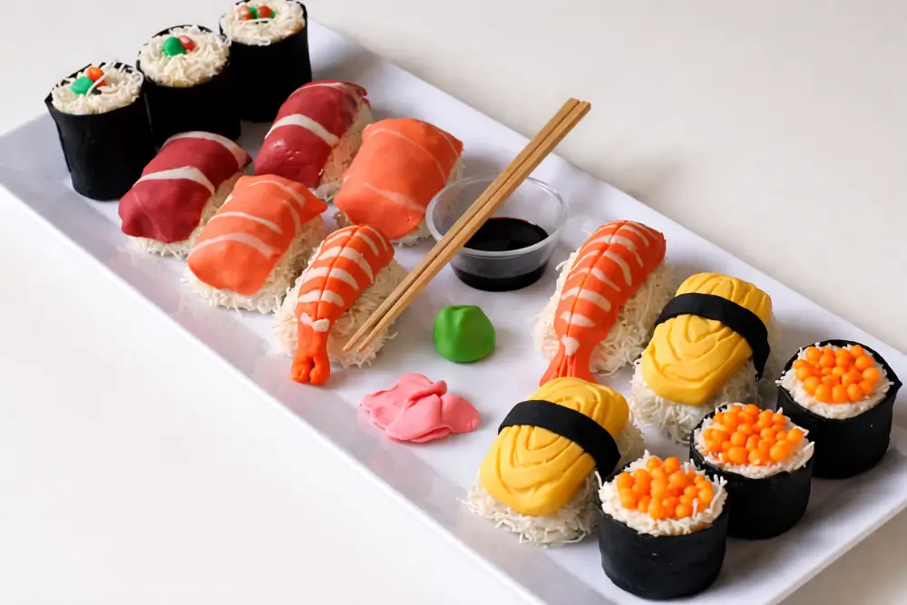 Sweet sushi platter arranged with fondant toppings, coconut-coated rolls, and chopsticks on the side.