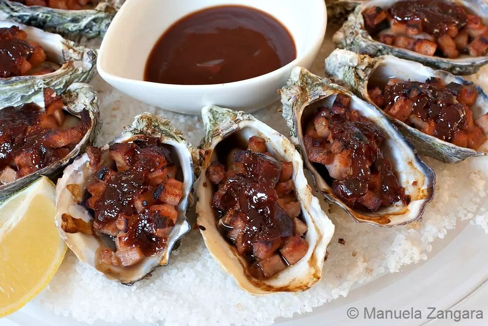 Close-up view of grilled Oysters Kilpatrick topped with crispy bacon and rich sauce.