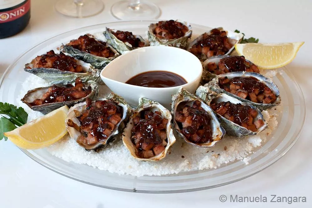Cooked Oysters Kilpatrick served on a round plate with Kilpatrick sauce and lemon wedges.