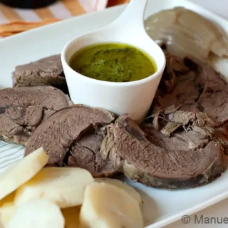 Sliced boiled beef served with carrots, potatoes, and a small bowl of Salsa Verde.
