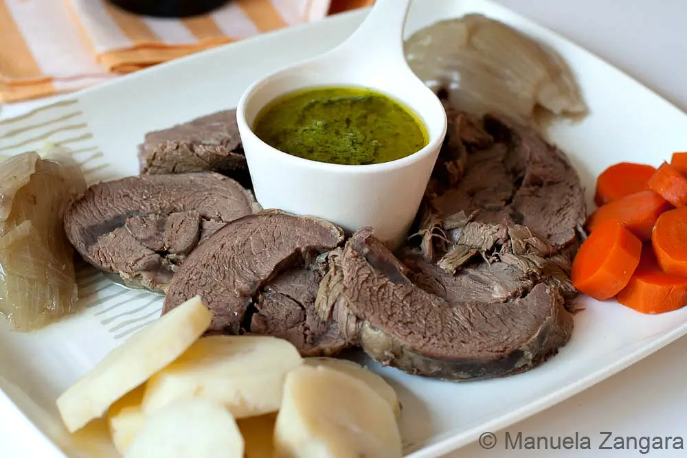 Sliced boiled beef served with carrots, potatoes, and a small bowl of Salsa Verde.