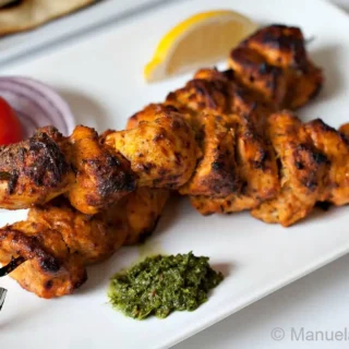 Cooked chicken tikka skewers served with chutney, lemon, and onions.
